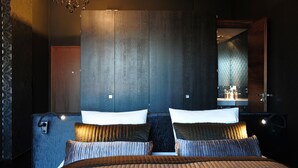 A modern hotel room with a large bed, dark wood paneling, and a mirror reflecting the room.