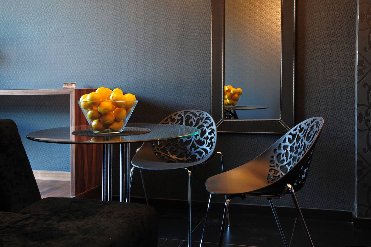 A modern room with a round glass table, a bowl of fruit, and two intricately designed chairs.