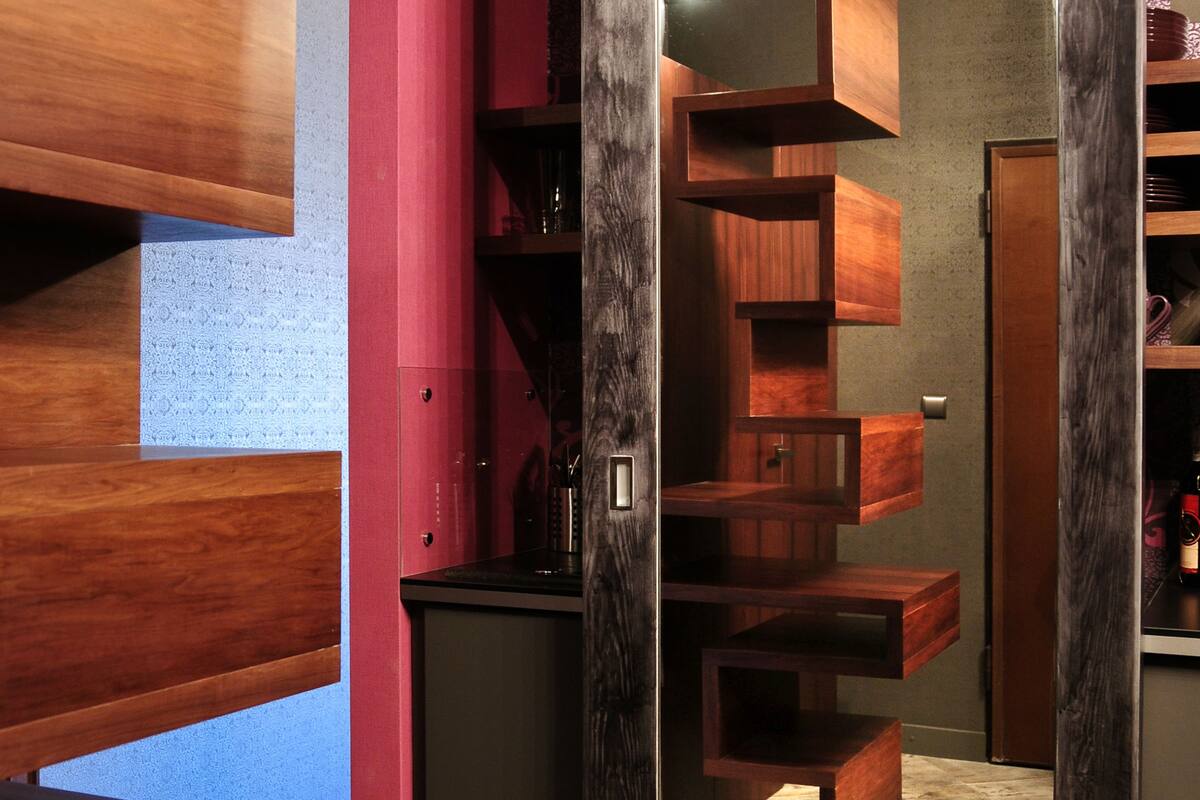 A modern interior with a wooden staircase, a black cabinet, and a mirror reflecting a wooden shelving unit.