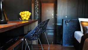 A modern hotel room with a wooden desk, a bowl of lemons, a black chair, and a bed with a white comforter.