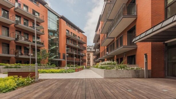 A modern apartment building with multiple balconies, a central courtyard with greenery, and a wooden deck area.