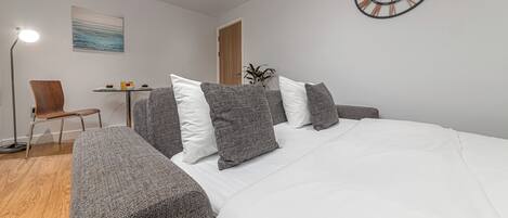 A modern bedroom with a large bed, a desk, a chair, and a wall clock.