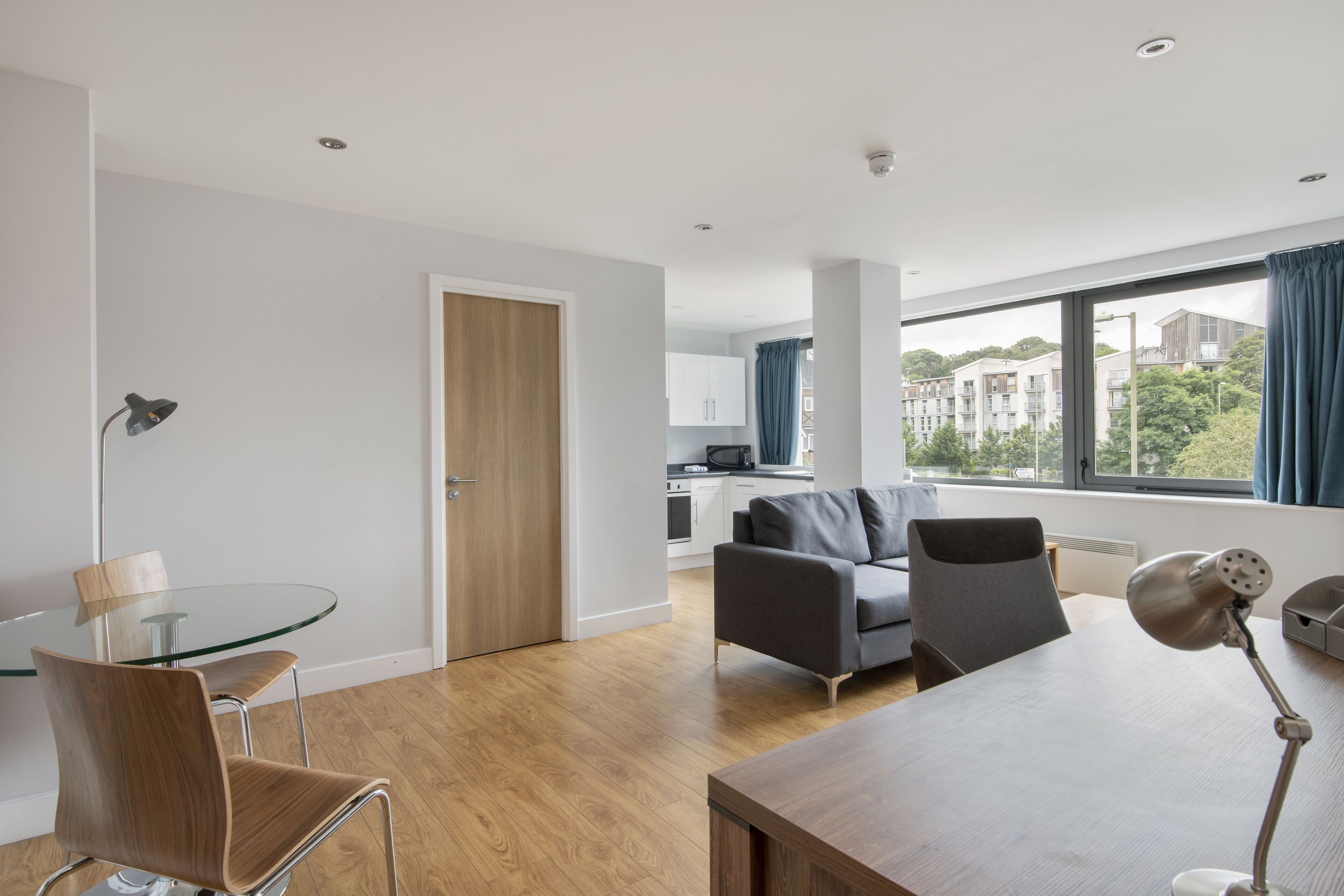 A modern living room with a glass dining table, two chairs, a sofa, and a lamp.