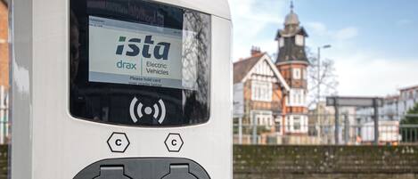 A white electric vehicle charging station with a digital display, two charging ports, and a logo.