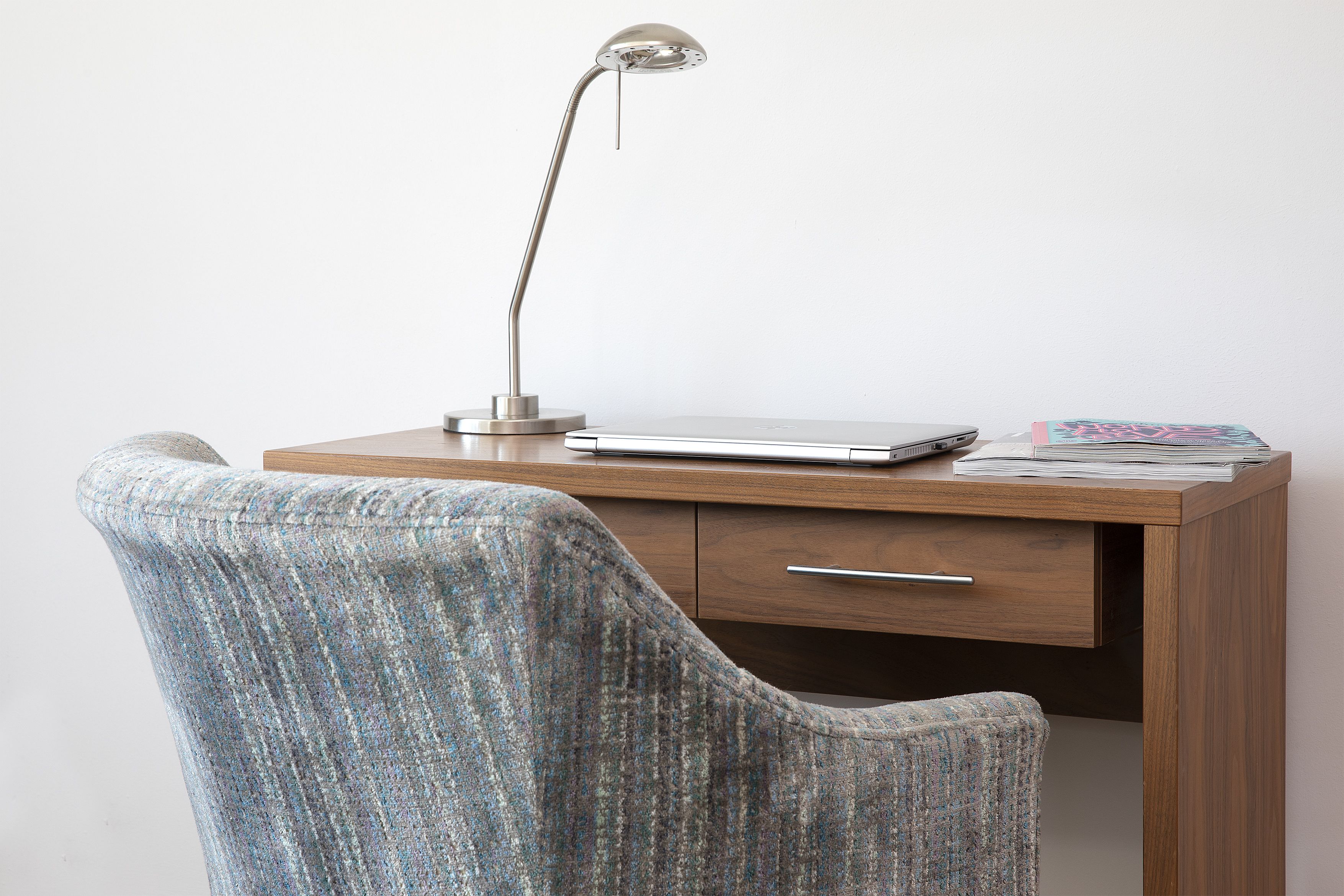 A wooden desk with a laptop, a metallic desk lamp, and a stack of papers.