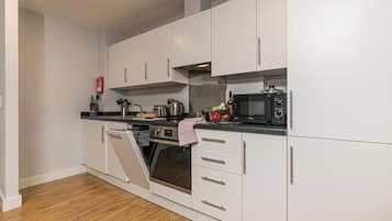 Una cocina moderna con armarios blancos, horno integrado, microondas y tostadora.
