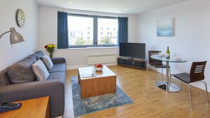 A modern living room with a sofa, coffee table, TV, and dining area. - HQ Aparthotel Farnborough (Farnborough)