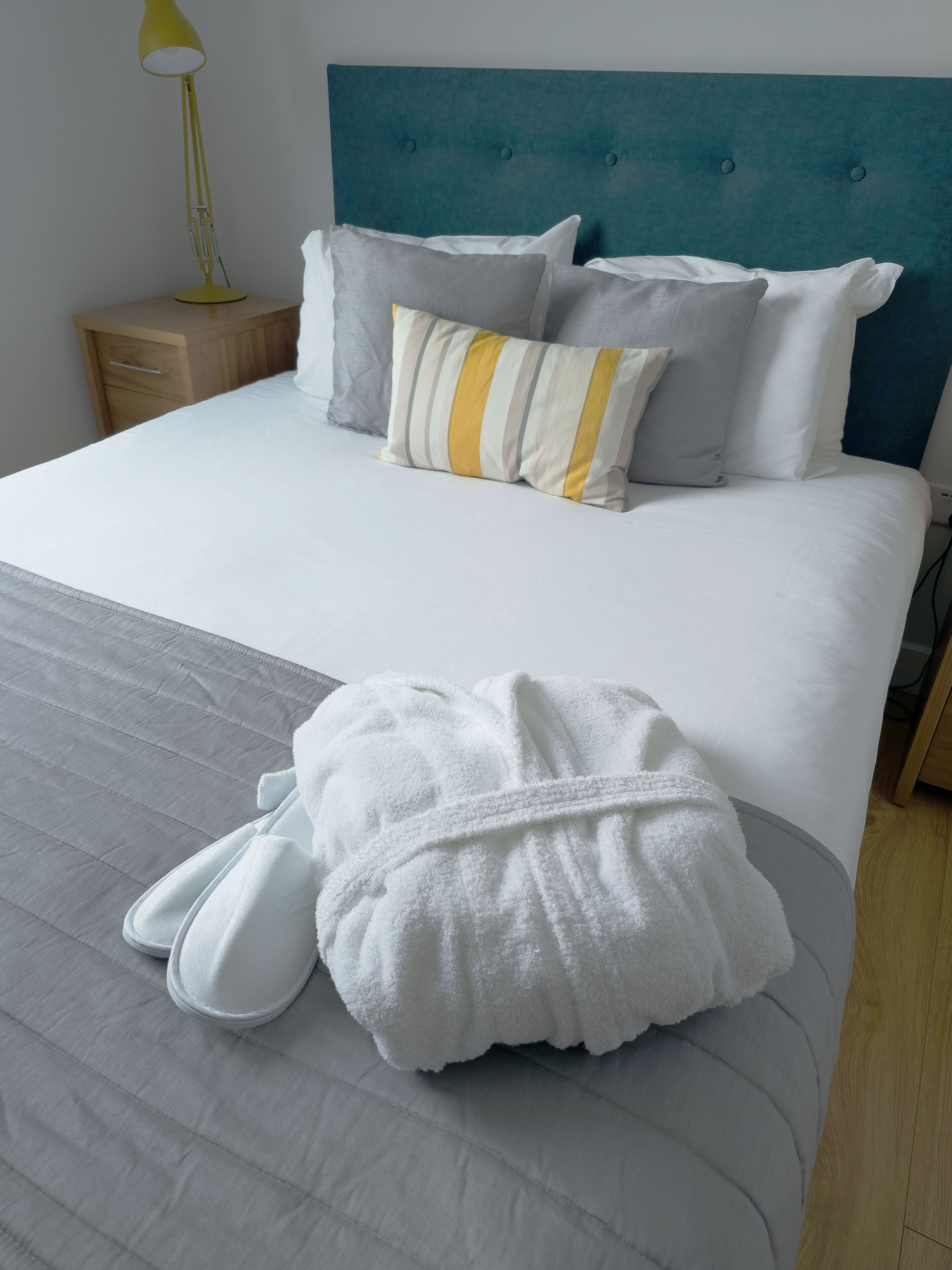 A neatly made bed with a grey and white striped duvet, a teal headboard, and several pillows in white, grey, and striped patterns.