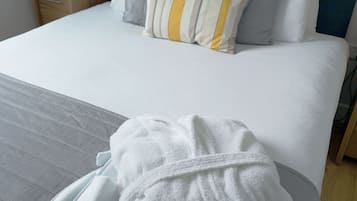 A neatly made bed with a grey and white striped duvet, a teal headboard, and several pillows in white, grey, and striped patterns.