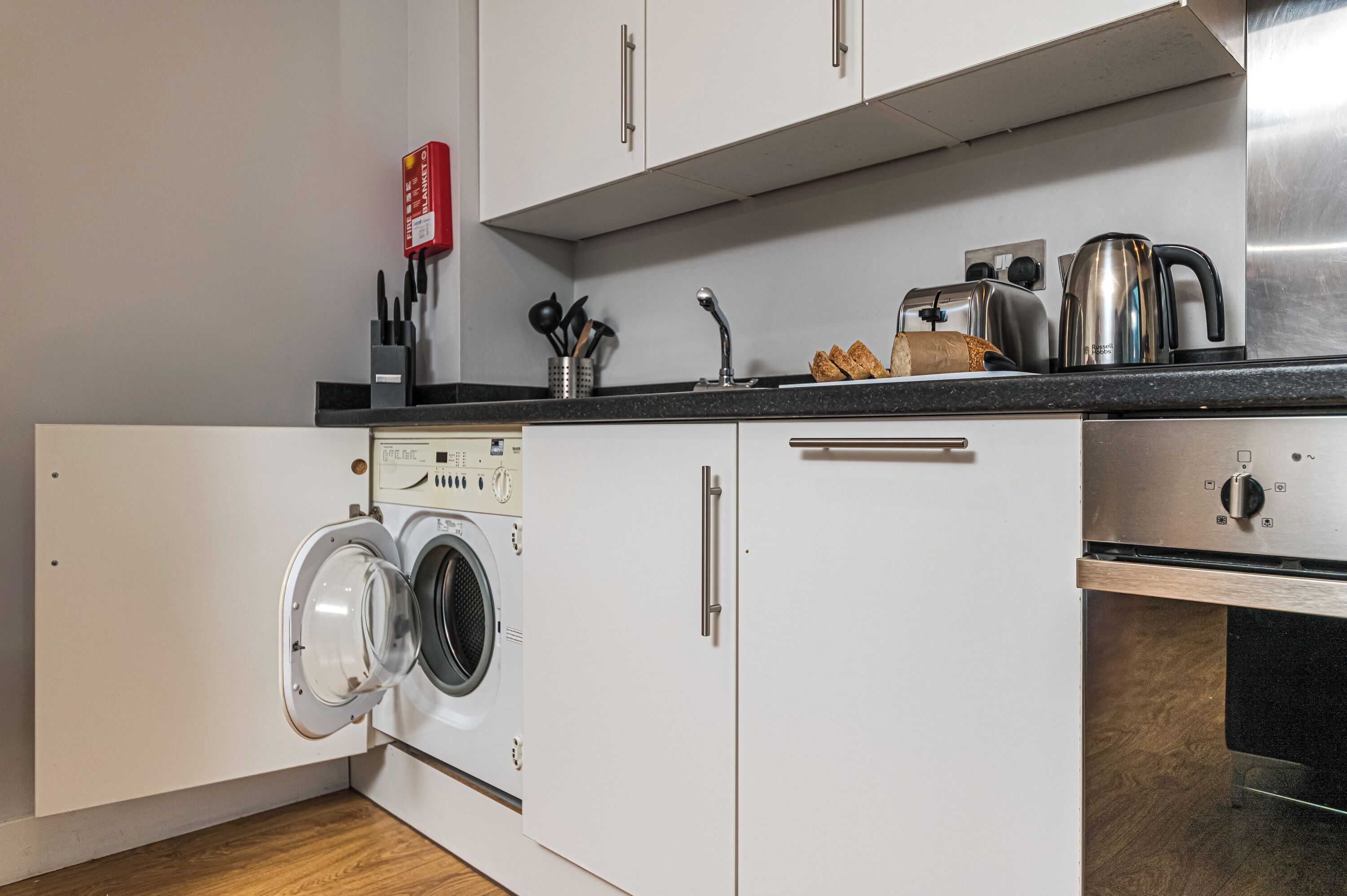 A compact kitchen with a built-in washer and dryer, stainless steel appliances, and a countertop with a toaster and kettle.
