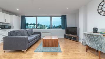 Una sala moderna con un sofá gris, una mesa de centro de madera y un televisor.