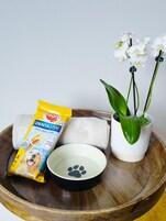 A wooden tray with a pet food bag, a white bowl with a paw print, and a potted orchid.