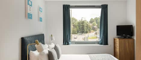 A hotel room with a bed, a desk with a lamp, a television, and a window with curtains.
