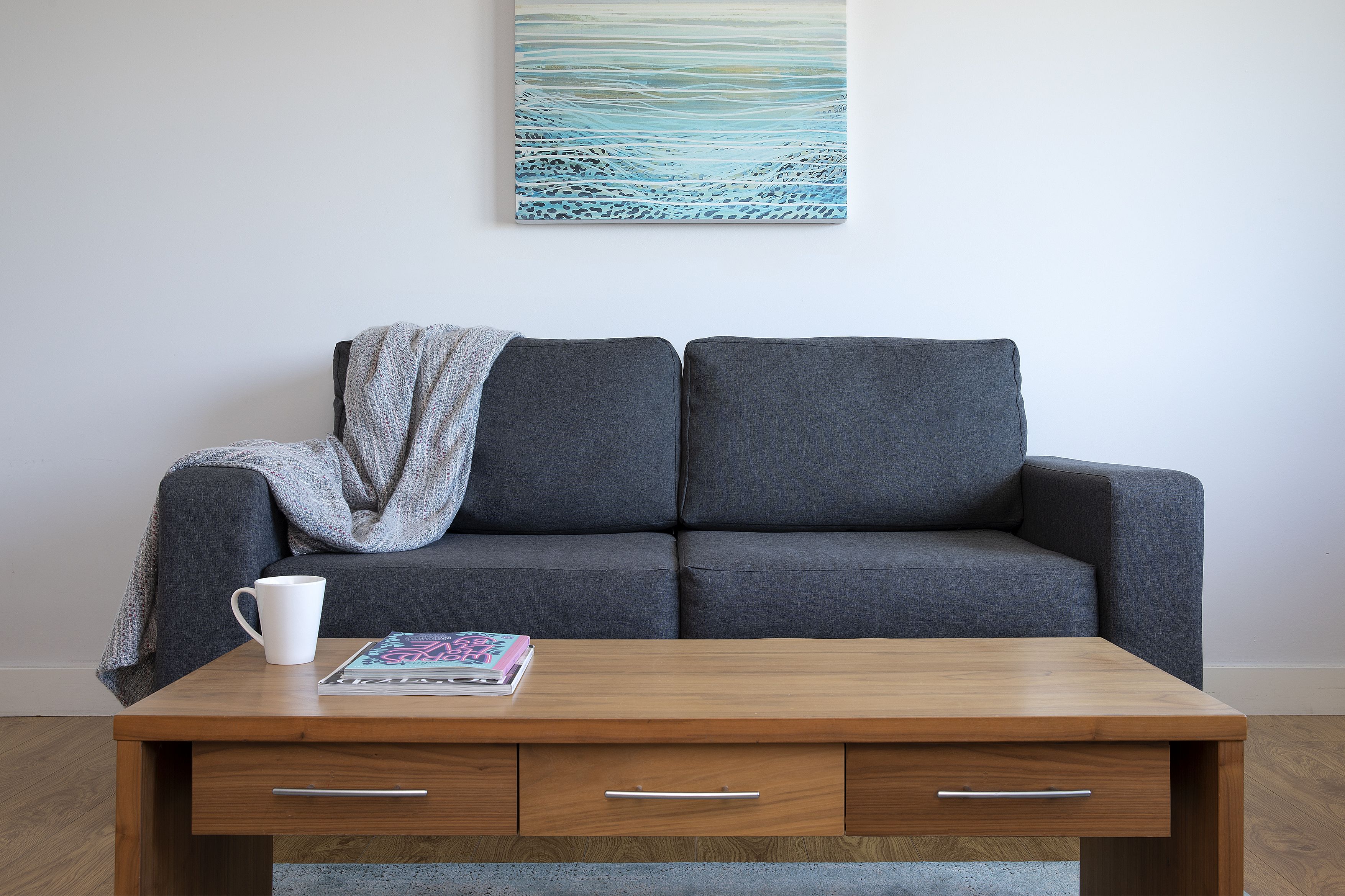 A modern living room with a grey sofa, a wooden coffee table with a magazine, and a white mug.