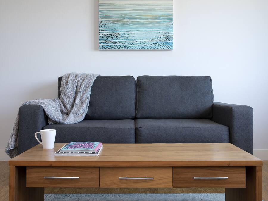 A modern living room with a grey sofa, a wooden coffee table with a magazine, and a white mug.