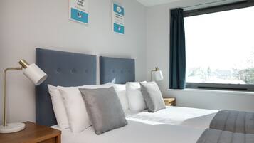 A neatly arranged hotel room with a large bed, two bedside tables, a desk, and a window with curtains.