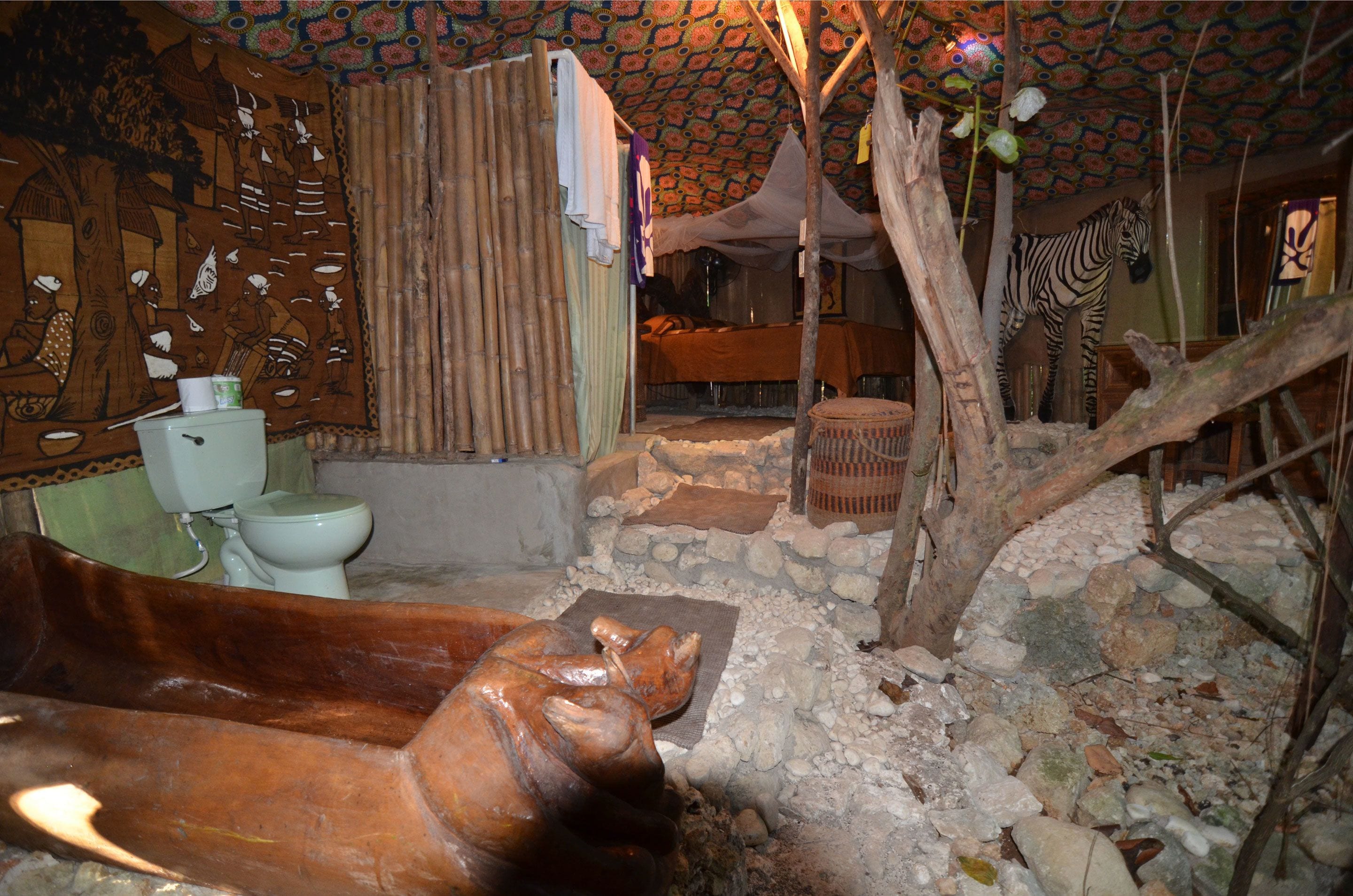 A rustic bathroom with a wooden bathtub, a toilet, and a zebra statue.