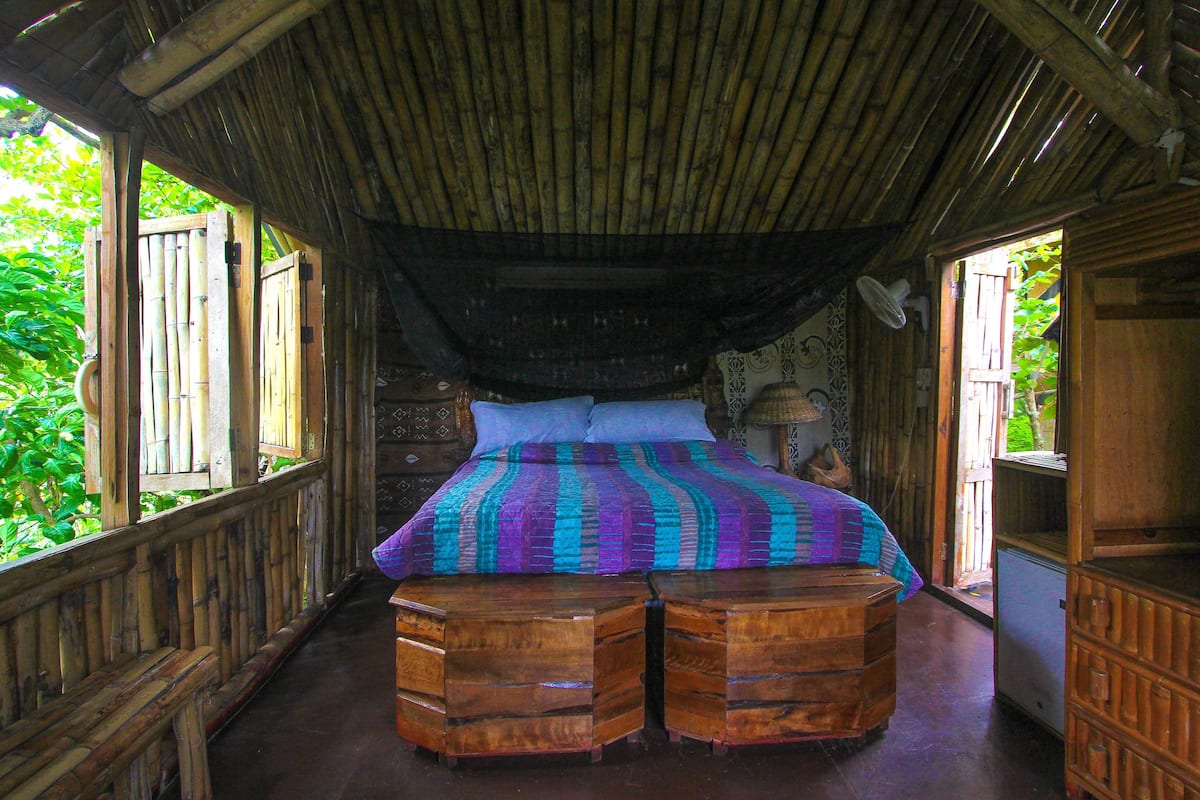 A room with a bed, wooden furniture, and a bamboo ceiling.