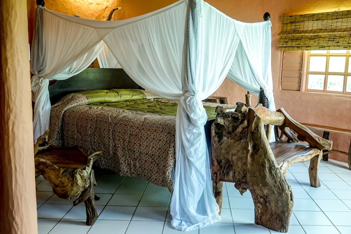 A room with a canopy bed, rustic wooden furniture, and a window with blinds.