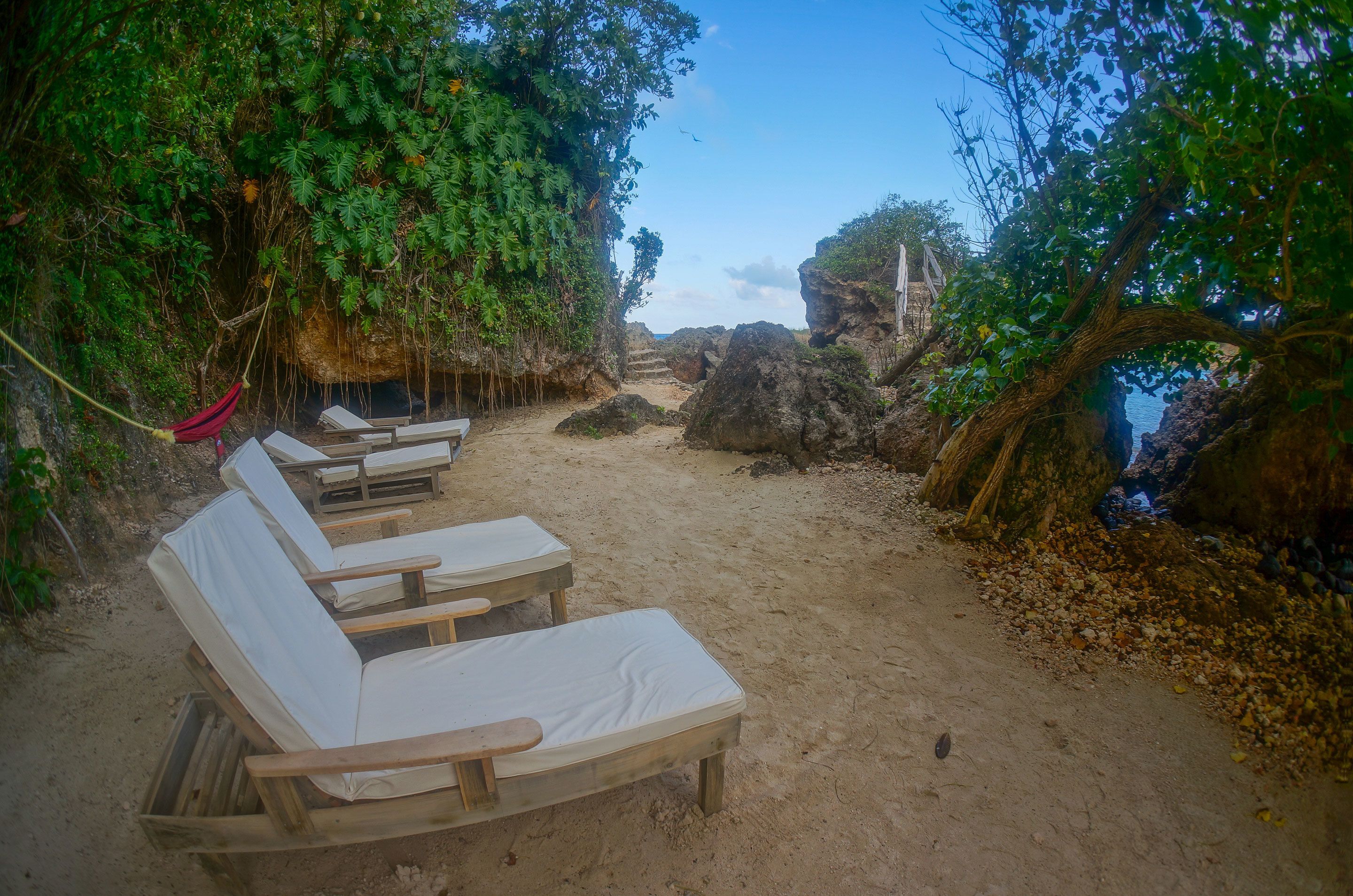 A sandy beach area with wooden lounge chairs and a hammock.