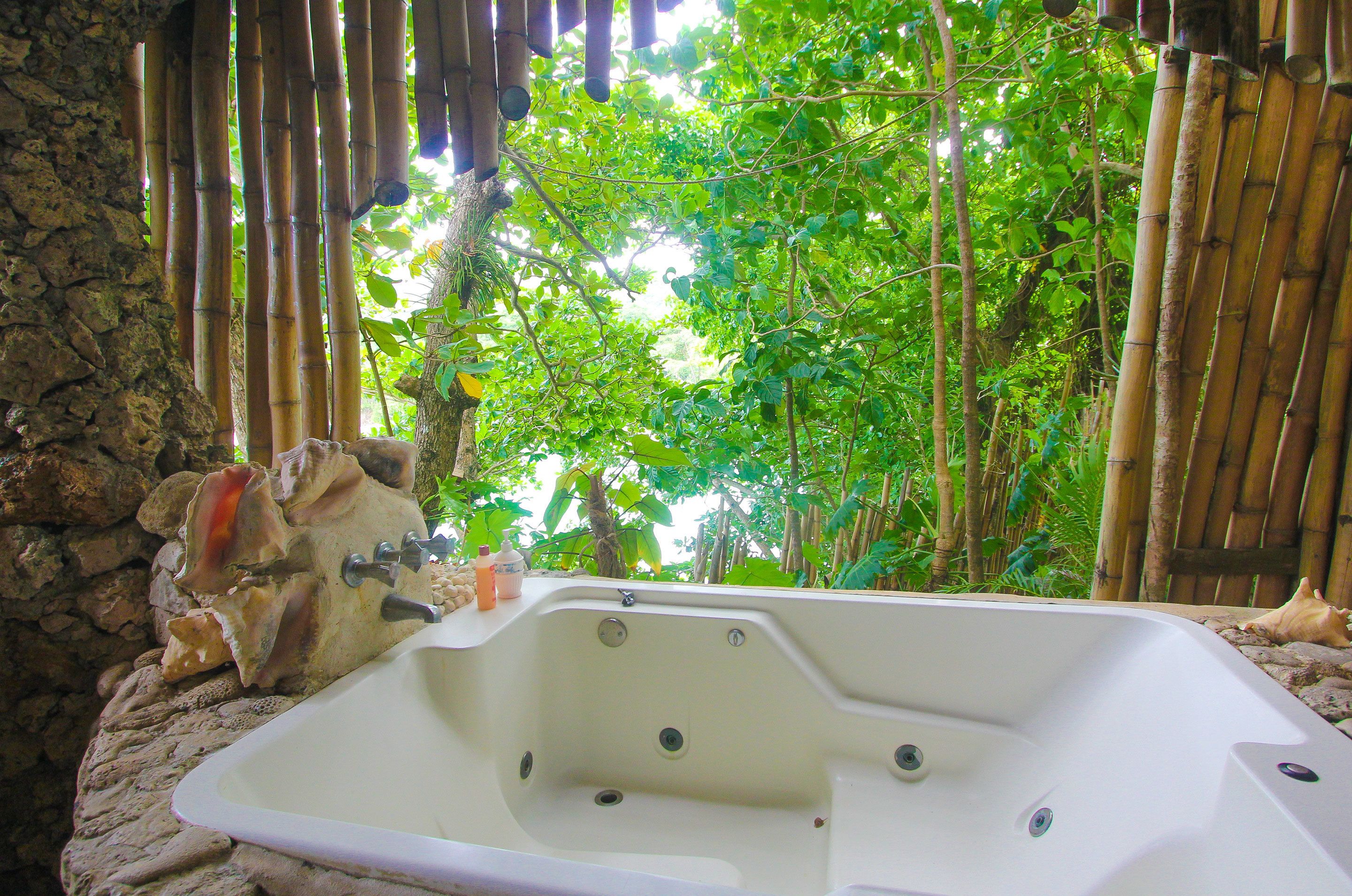 Una bañera de hidromasaje en un entorno natural, con paredes de bambú y suelo de piedra.