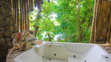 Una bañera de hidromasaje en un entorno natural, con paredes de bambú y suelo de piedra.