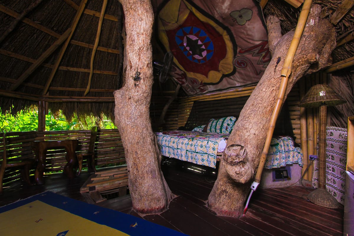 A treehouse bedroom with a bed, wooden furniture, and a thatched roof.