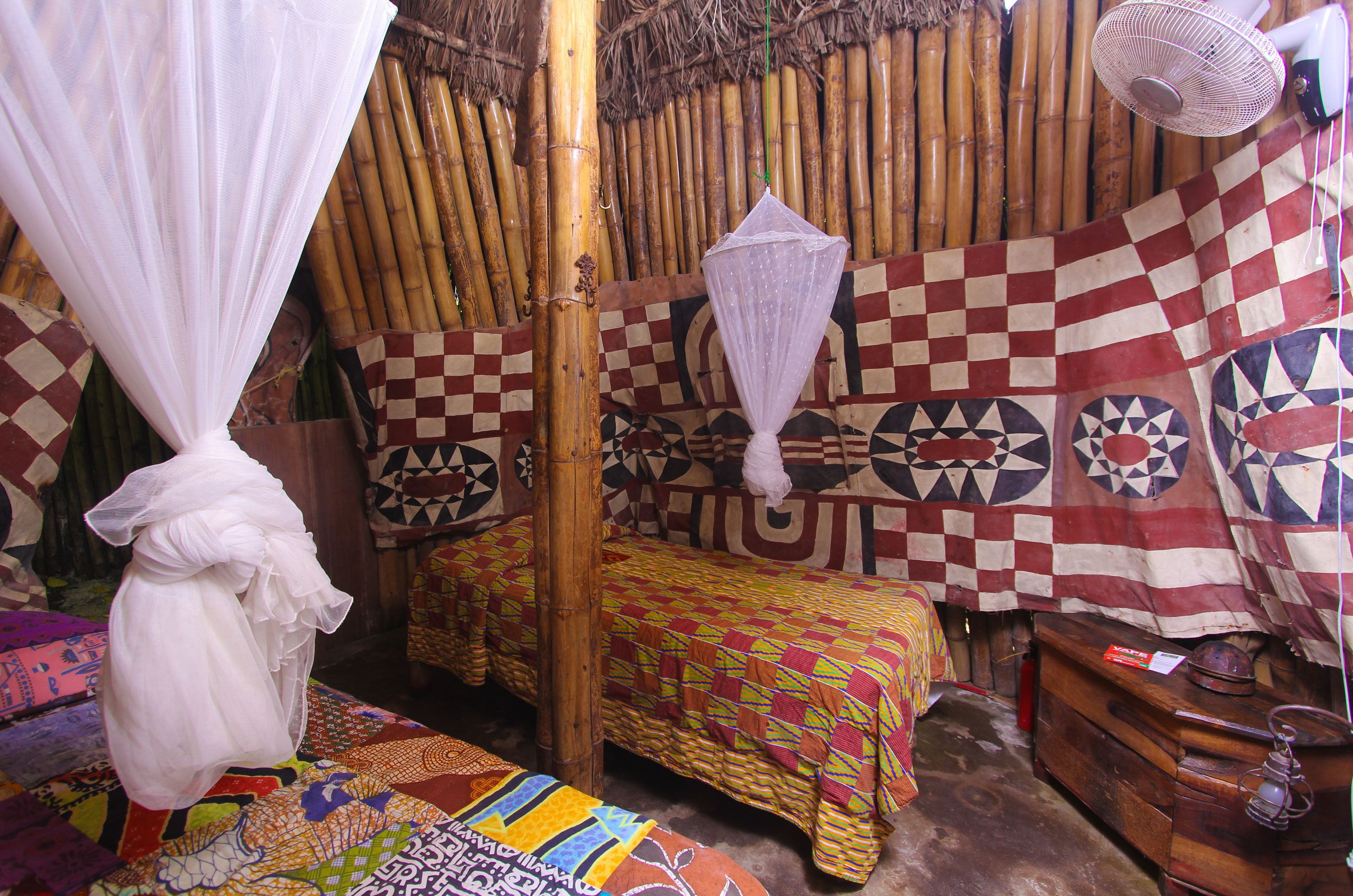 A room with a checkered bedspread, a wooden dresser, and a mosquito net.