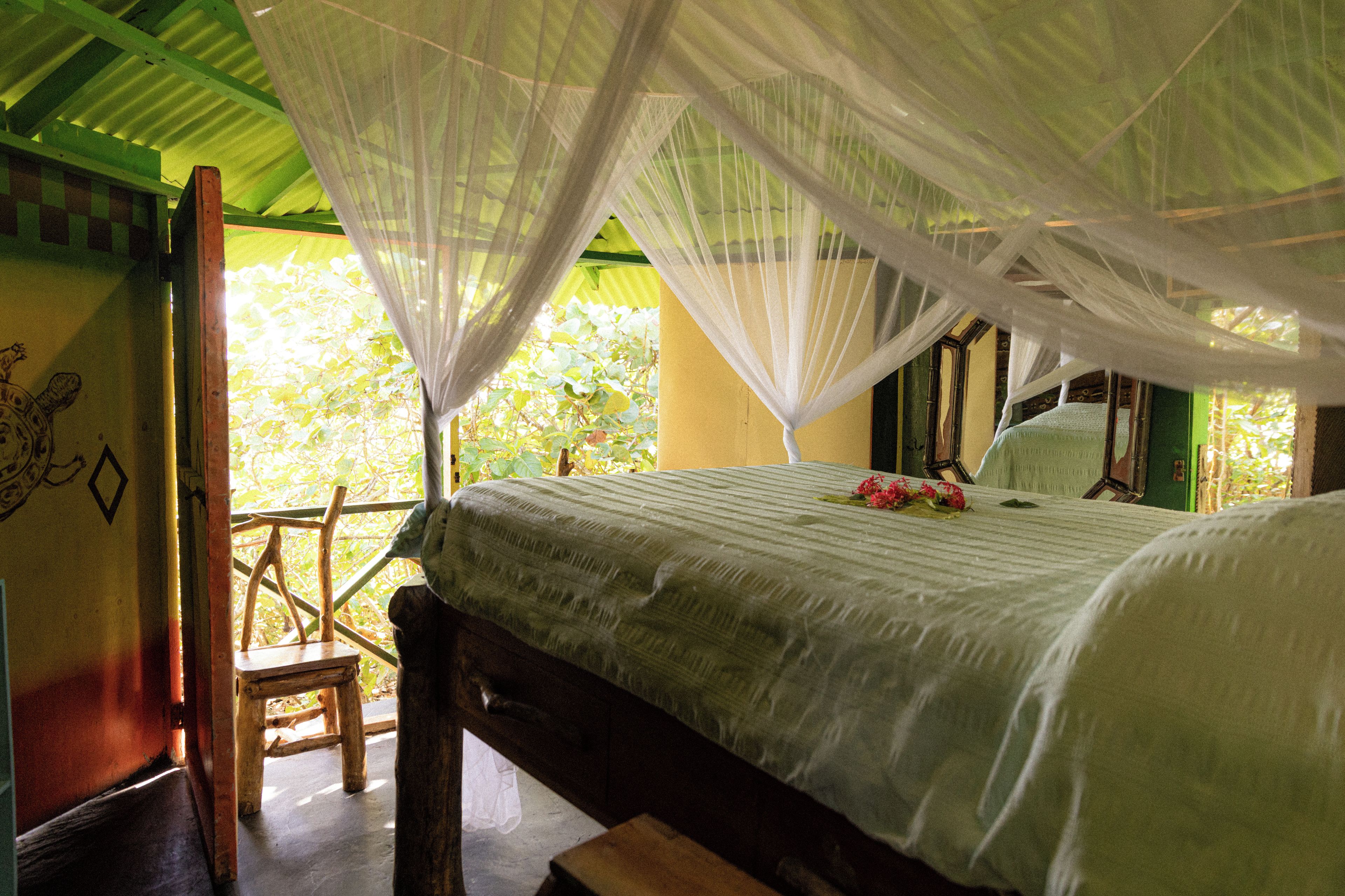 A room with a bed under a canopy, a wooden chair, and a view of greenery outside.