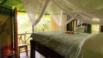 A room with a bed under a canopy, a wooden chair, and a view of greenery outside.
