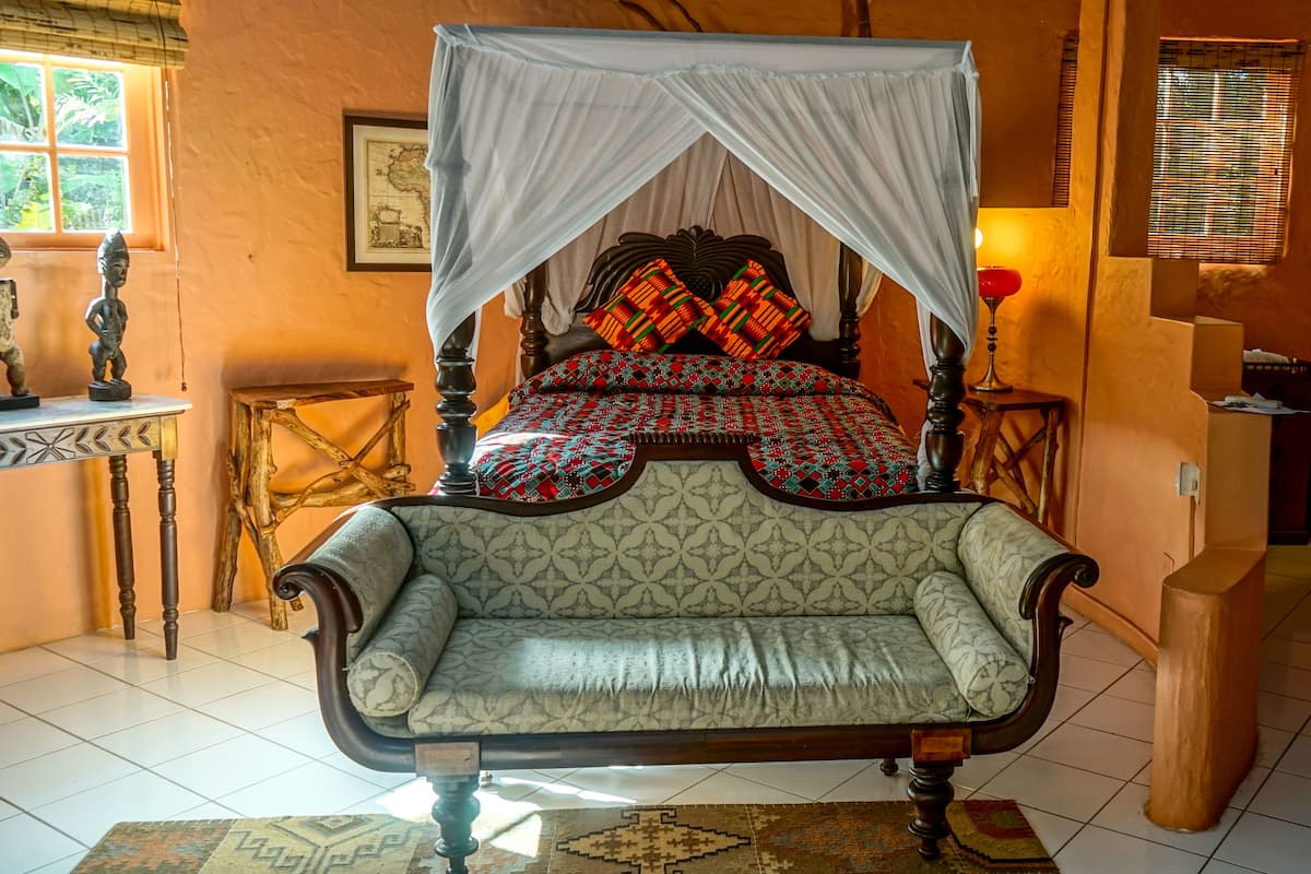 A room with a bed under a canopy, a sofa, a small table, and a lamp.