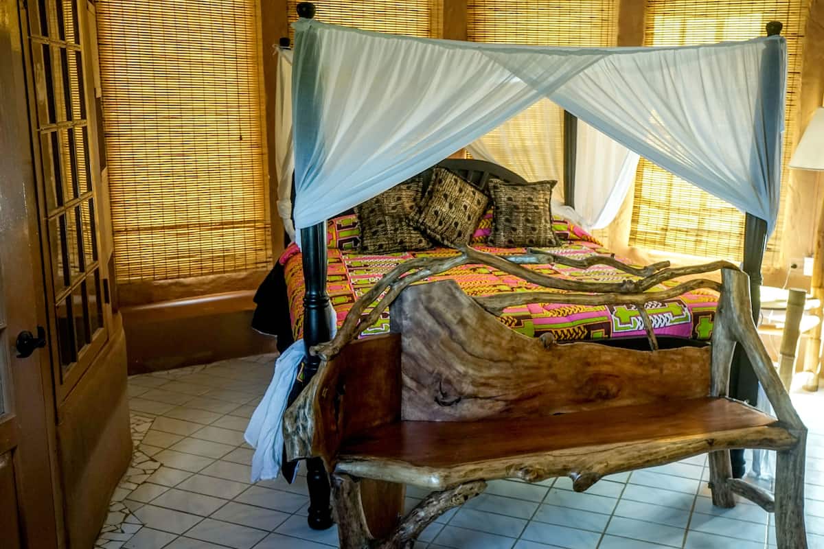 A bed with a canopy, a wooden bench, a chair, and a lamp.