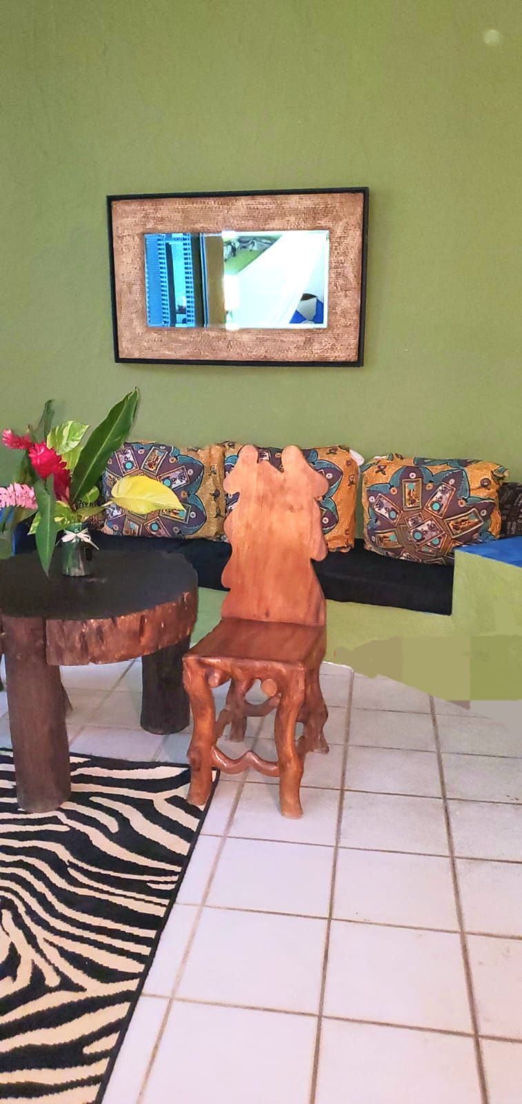 Una habitación con una silla de madera, una mesa redonda con un jarrón de flores, un tapete estampado de cebra y un sofá con cojines decorados.
