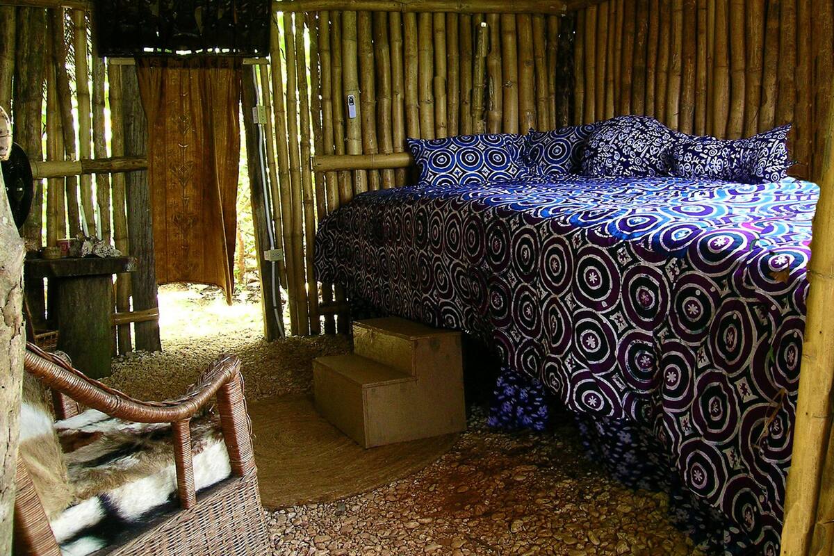 A room with a bed, a chair, and a small wooden stool.