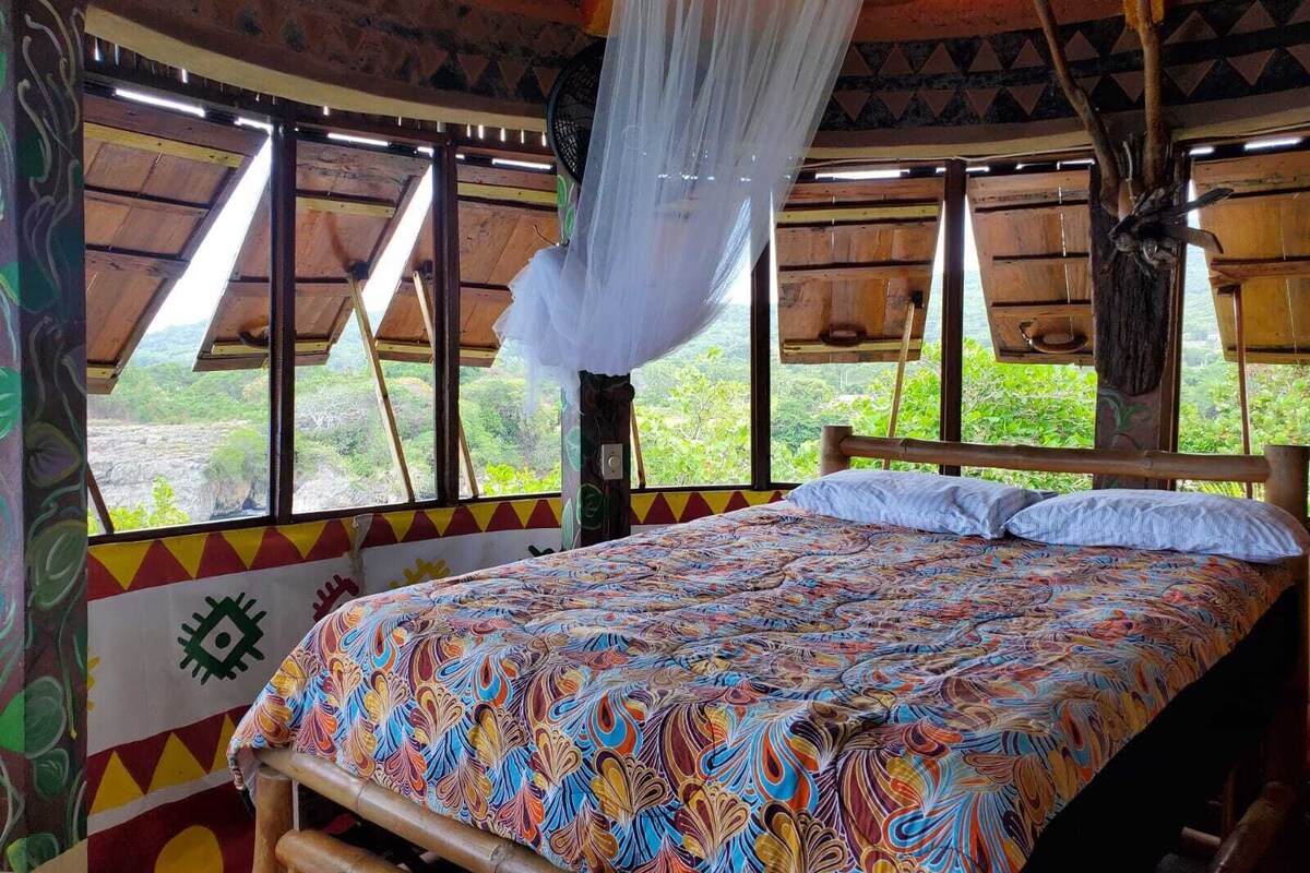 Une chambre avec un lit, une moustiquaire et de grandes fenêtres donnant sur un paysage.