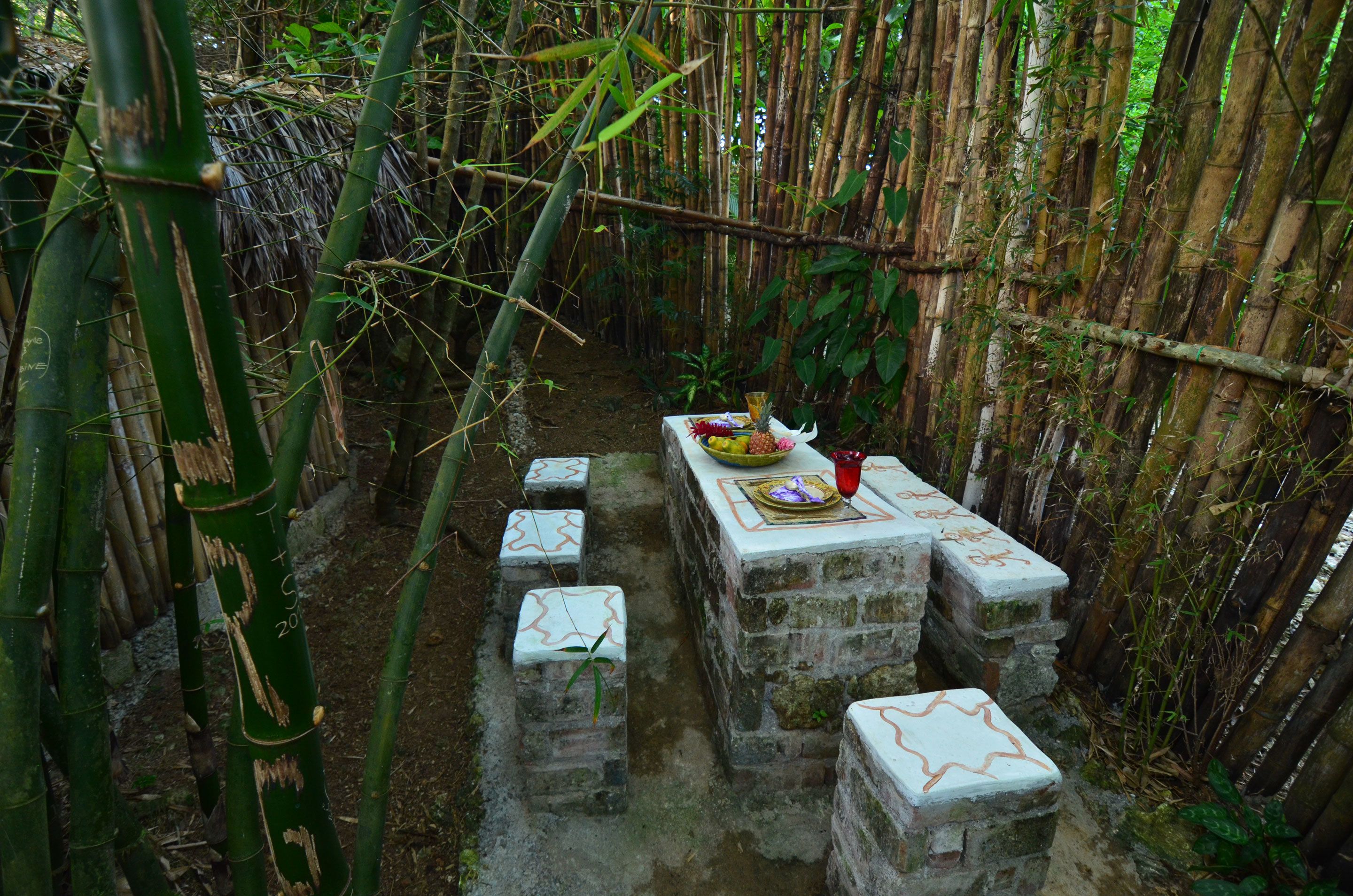 A narrow bamboo-lined pathway with stone steps leading to a table set with food and a red object.