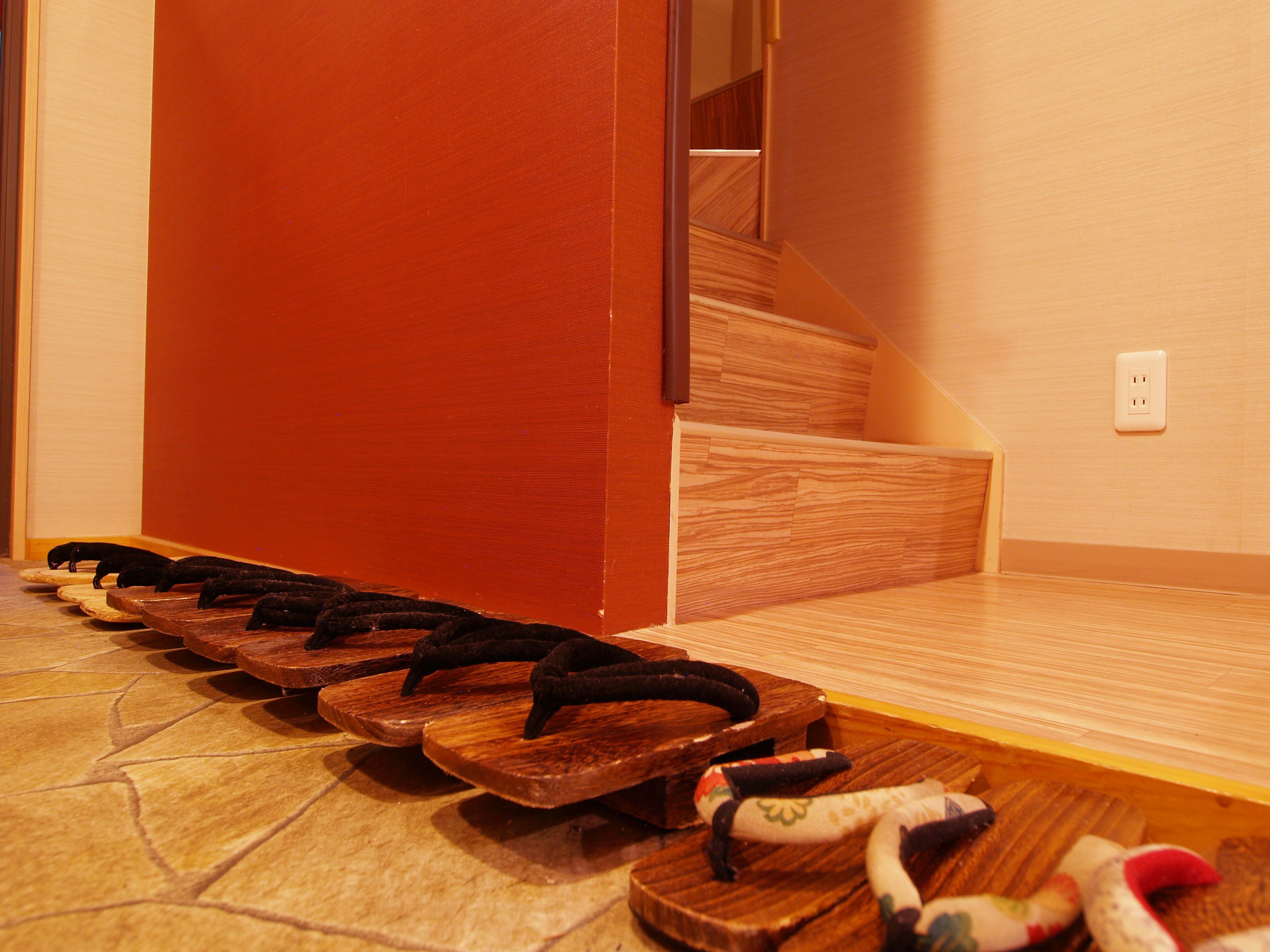 A row of wooden sandals on a tiled floor near a staircase.