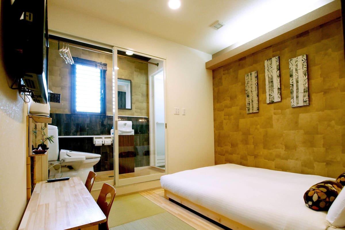 A bedroom with a bed, a desk, and a bathroom with a toilet and sink.