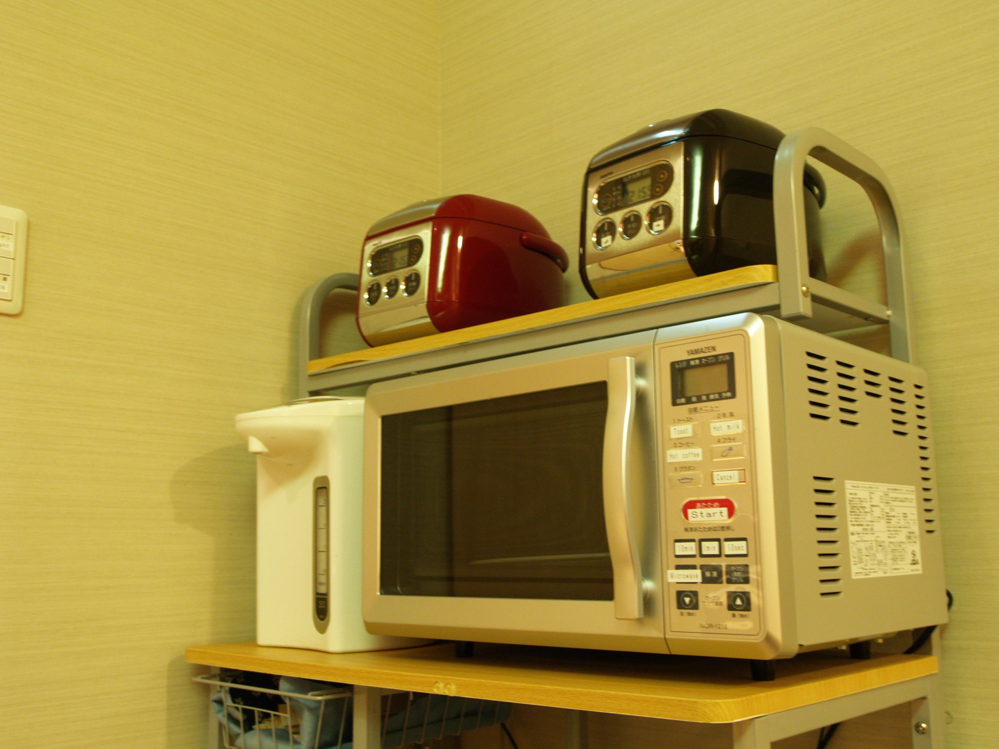 A microwave oven with a digital display and control panel, placed on a wooden shelf.