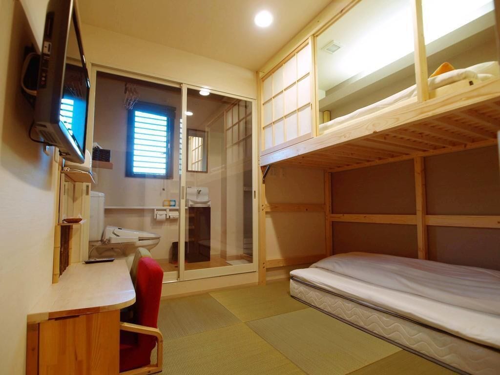 Une chambre compacte comprenant un lit superposé, un bureau avec une chaise, une télévision et une porte coulissante donnant accès à une salle de bain.