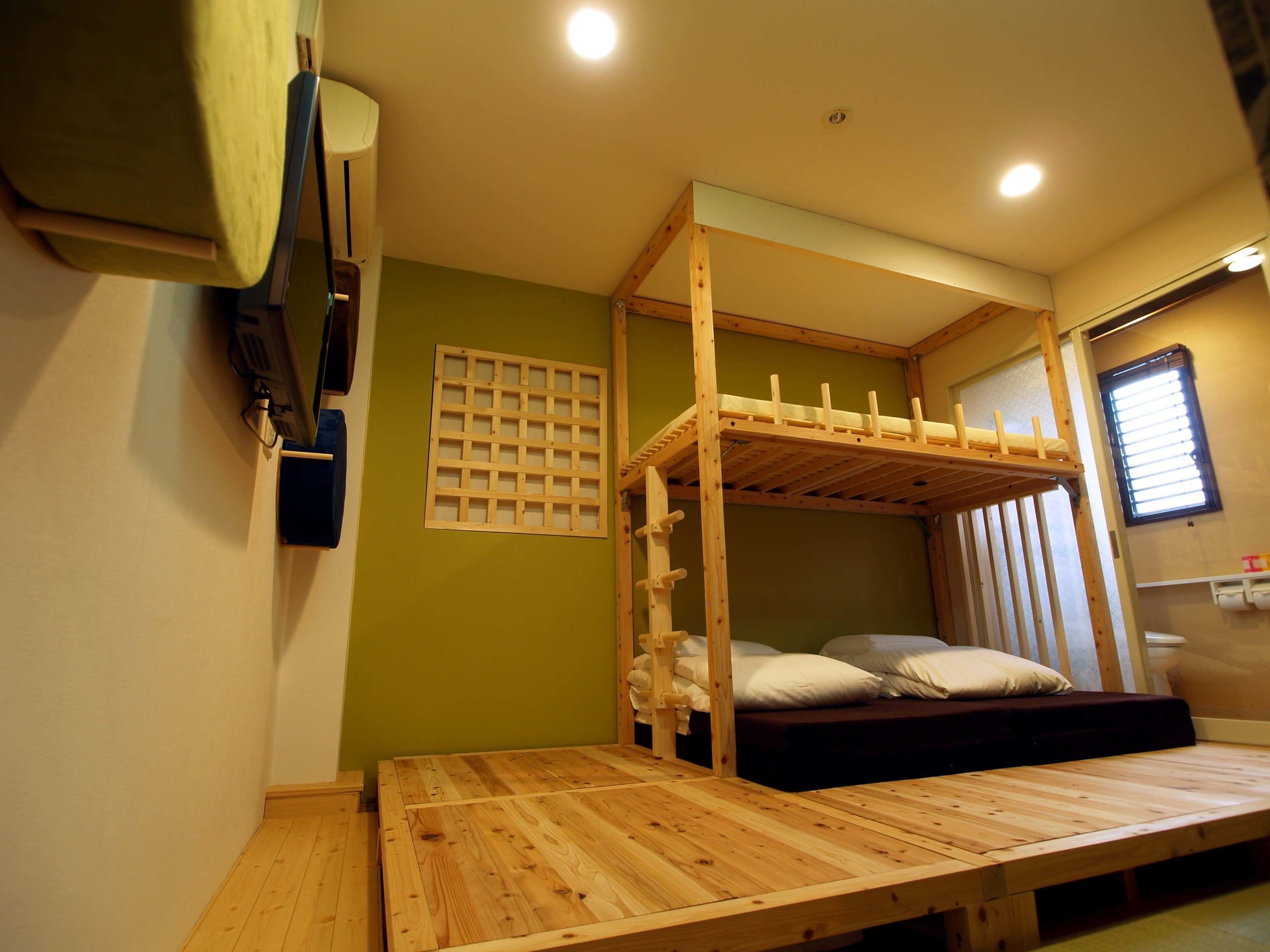 Een stapelbed met een houten frame, een klein tafeltje en een raam met blinds.