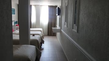 Et hotelværelse med tre senge langs væggen, et lille håndvaskområde og et fjernsyn monteret på væggen.