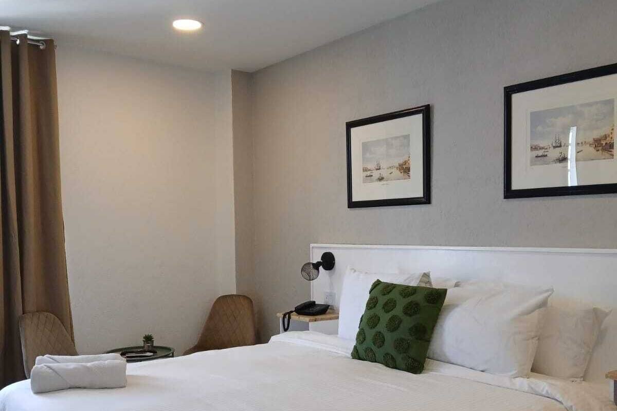 Ein Hotelzimmer mit einem großen Bett, einem Sessel, einem Nachttisch mit Lampe und zwei gerahmten Bildern an der Wand.