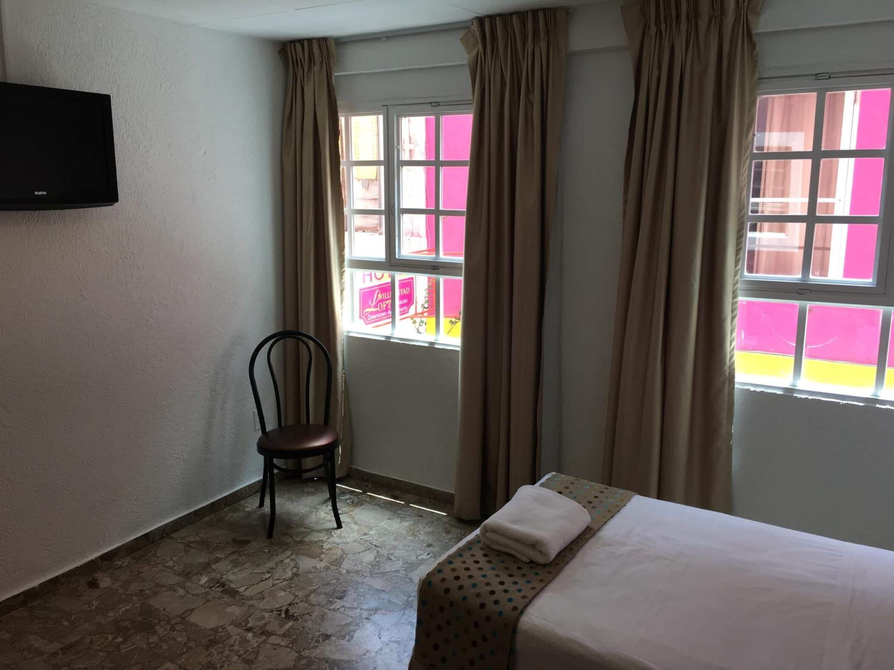 A room with a bed, a chair, and a television on the wall.