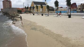 Una spiaggia con un edificio giallo dotato di torre, palme e alcune persone.