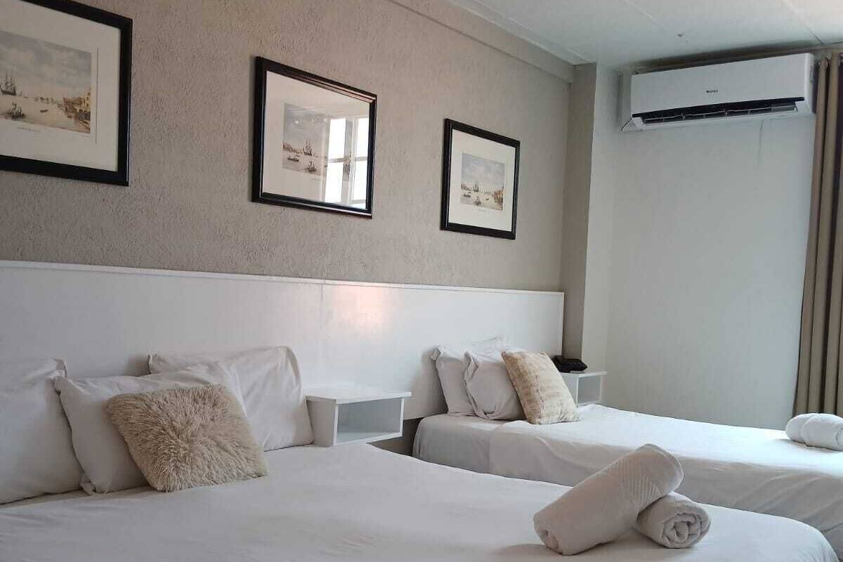 Ein Hotelzimmer mit zwei Betten, weißer Bettwäsche, einem Kopfteil, einem Nachttisch und gerahmten Bildern an der Wand.