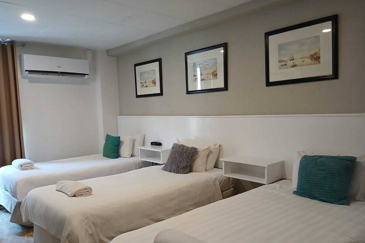 Ein Hotelzimmer mit zwei Einzelbetten, einem weißen Kopfteil, einem kleinen Nachttisch und einer Wand-Klimaanlage.