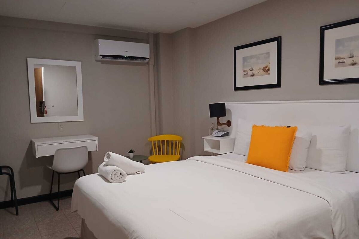 Ein Hotelzimmer mit Bett, Schreibtisch, Stuhl, Klimaanlage und einem kleinen Tisch mit Lampe.