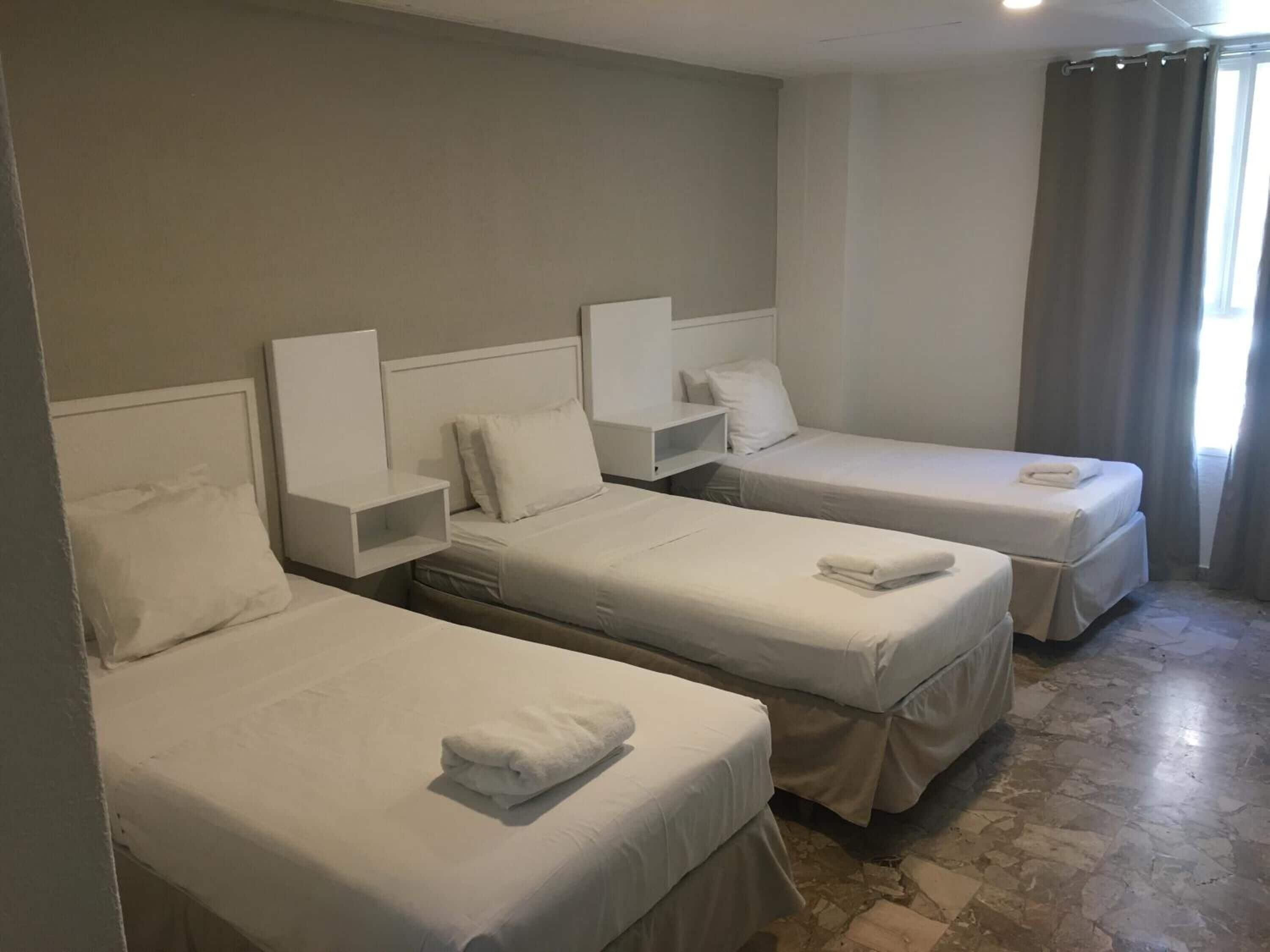 A hotel room with three single beds, each with a white headboard and bedside table.