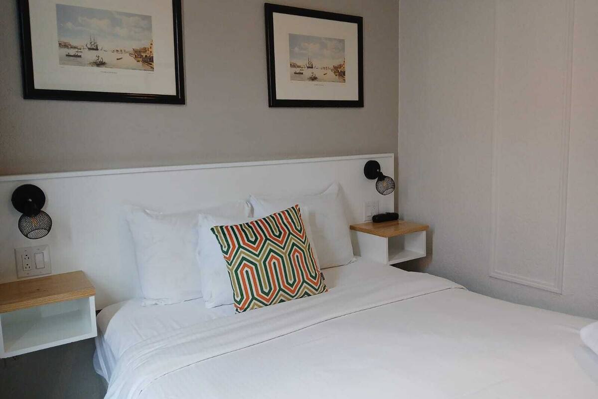 Ein ordentlich eingerichtetes Hotelzimmer mit einem Bett, zwei Nachttischen und zwei gerahmten Bildern an der Wand.